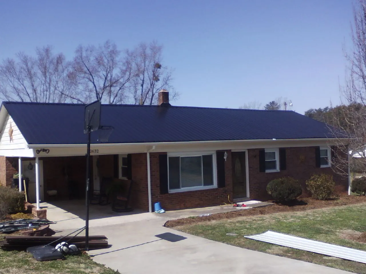Finished dark blue metal roof on a brick ranch with a carport in West Harwich