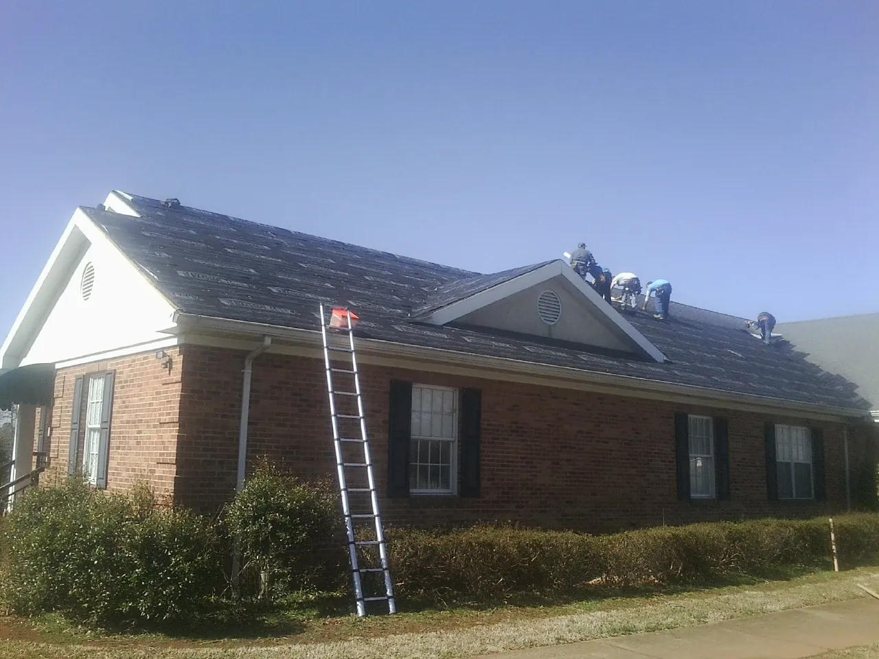 Crew tearing shingles off a brick ranch roof with a ladder set — Emergency Roof Repair work by our crew in West Harwich