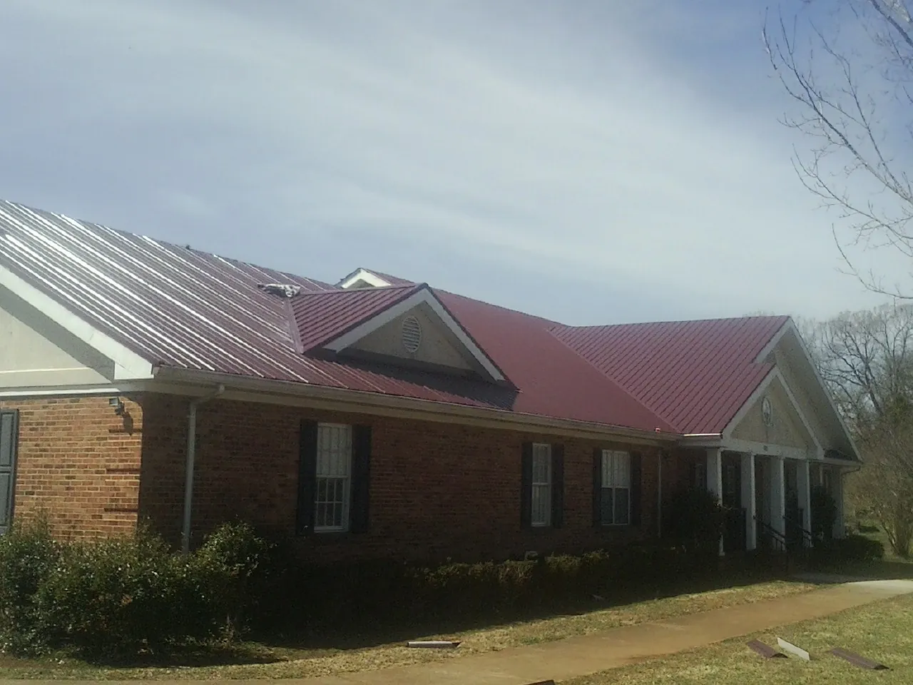 Red metal roof with gabled entries on a long brick building, from a Hail Damage Roof Repair job in West Harwich