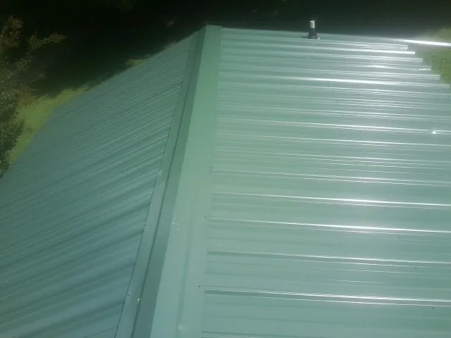 New green metal panels meeting at the ridge of a roof — Flat Roof Repair work by our crew in West Harwich