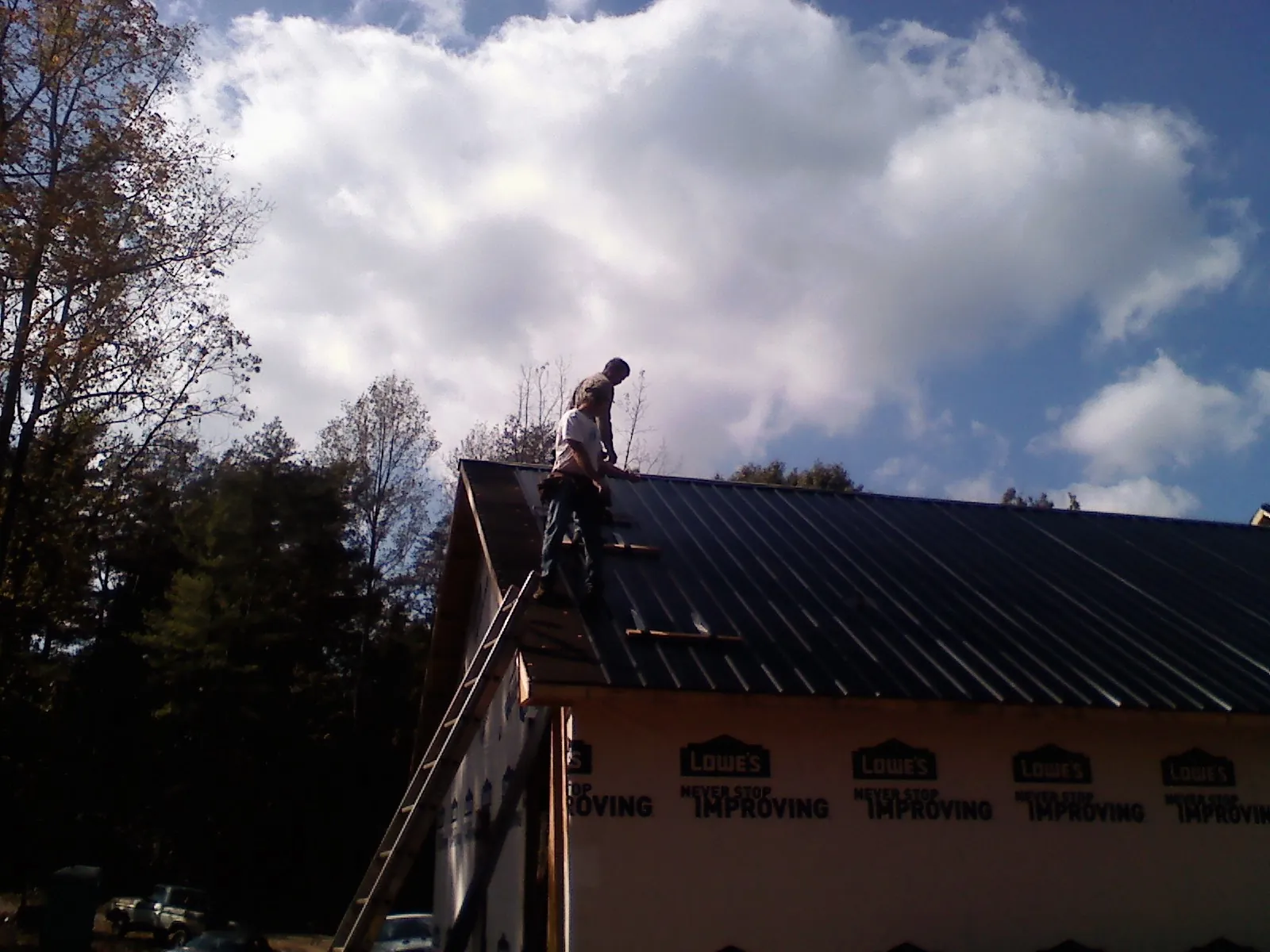 Roofer fastening dark metal panels high against a cloudy sky, from a Roof Inspection job in West Harwich