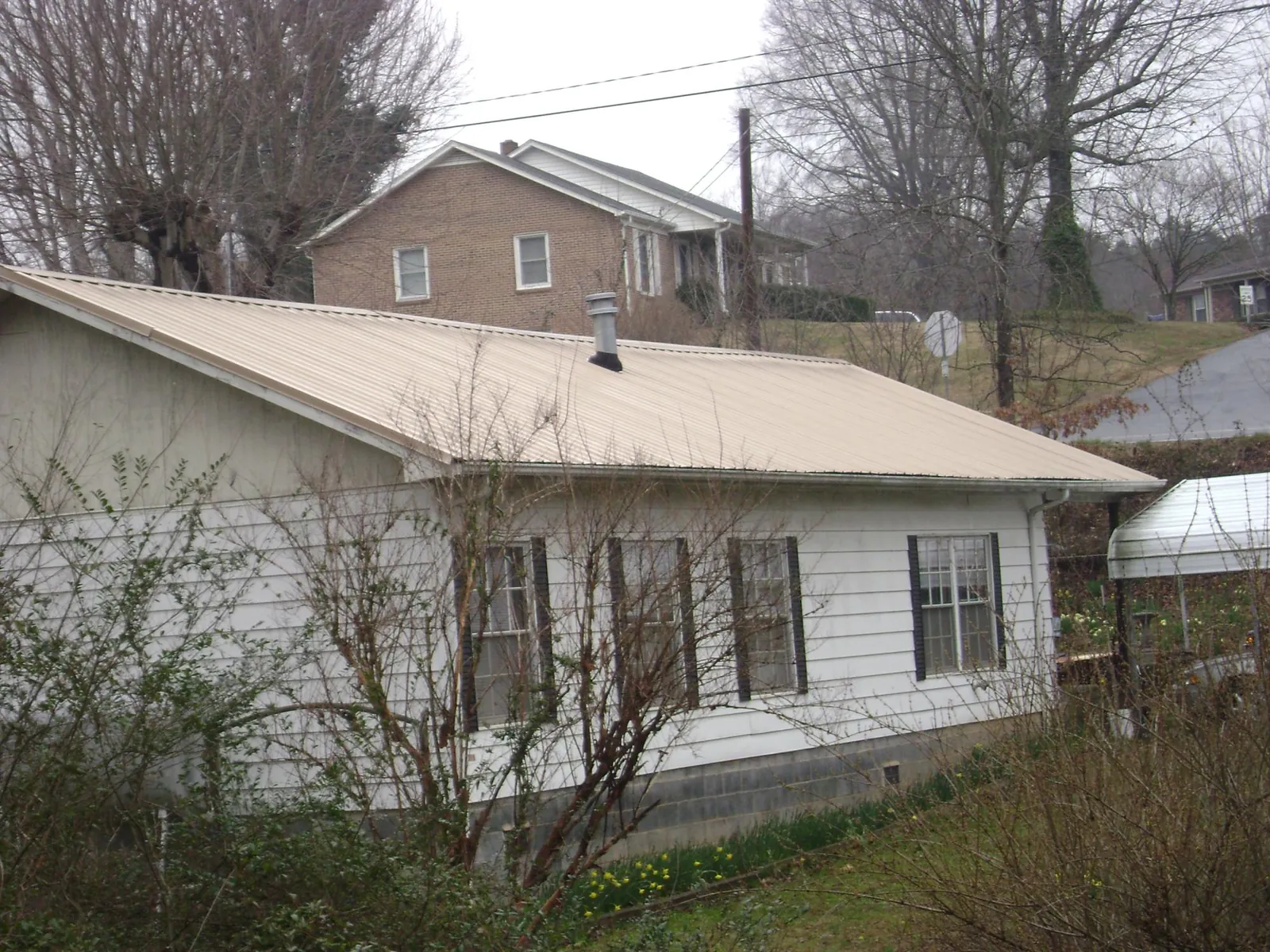 Tan metal roof on a white sided house set into a hillside — Commercial Roofing by Roofing Brothers in West Harwich